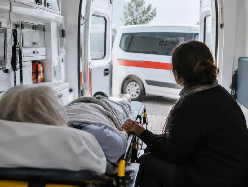 Hasta nakil ambulansında sedyedeki yaşlı hastanın elini tutan yakını